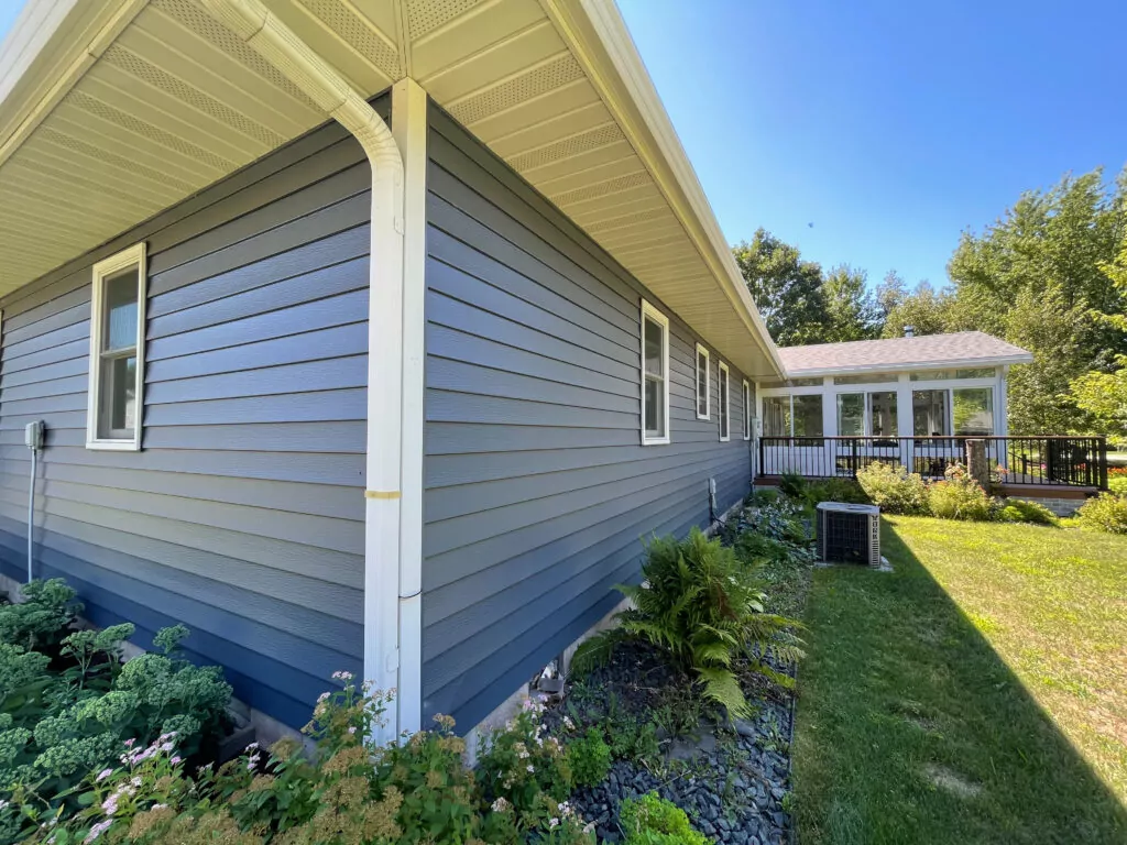 Home exterior featuring blue siding, white trim, and a well-maintained yard with greenery, illustrating the importance of proper home protection and maintenance for seasonal changes.