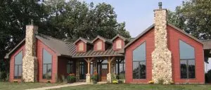 Modern home exterior featuring classic red siding, large windows, and stone chimneys, showcasing a blend of rustic charm and contemporary design, relevant to 2025 siding trends.